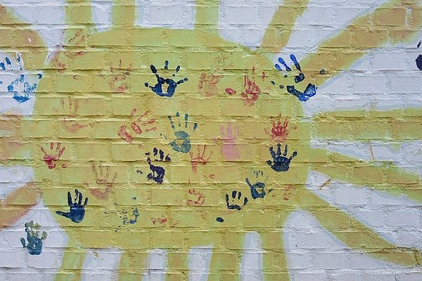 Gelbe Sonne an der Hauswand mit bunten Abdrücken von Kinderhänden