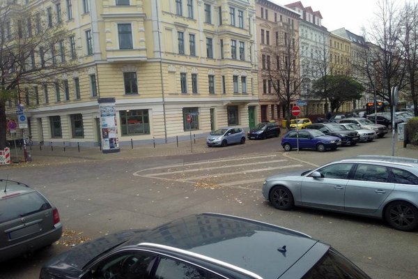 Straßenkreuzung mit zahlreichen parkenden Autos und einer aufgemalten Sperrfläche