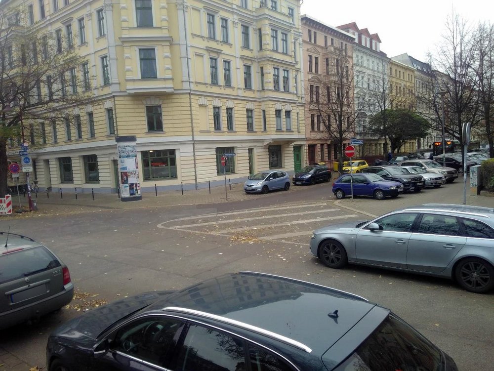 Straßenkreuzung mit zahlreichen parkenden Autos und einer aufgemalten Sperrfläche